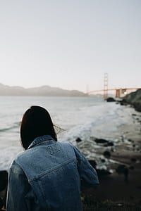 woman wearing blue denim jacket sitting on rock near seashore thumbnail