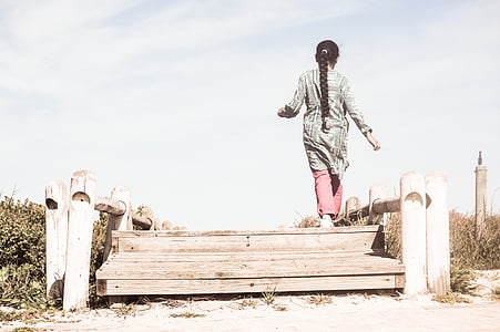 woman wearing black and white dress walking on brown wooden dock under blue sky thumbnail