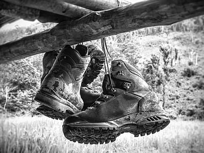 grayscale photo of hiking boots hanged under brown bamboo thumbnail