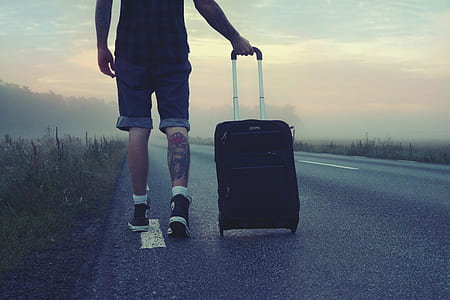 Man Walking on the Road Holding Black Luggage during Sunset thumbnail