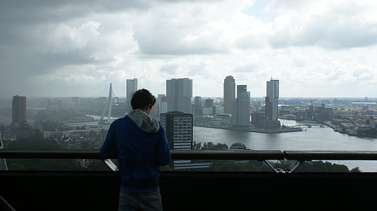 man wearing blue shirt holding hand rail viewing high rise building thumbnail
