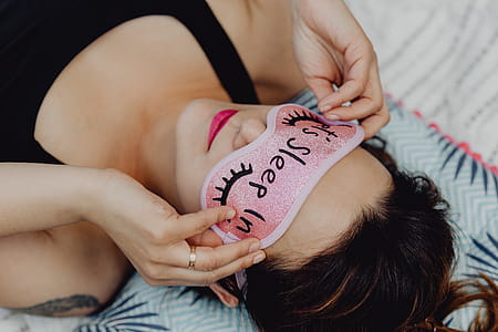 Joyful girl relaxing in bedroom - top view of brunette women in pink sleeping mask thumbnail