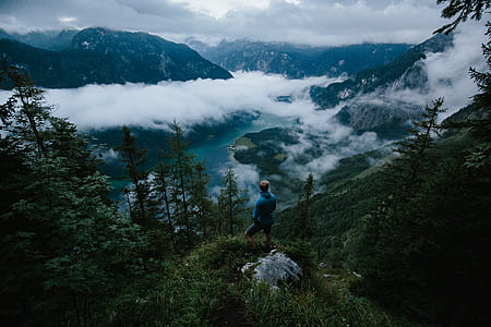 man standing on top of mountain under cloudy sky during daytime thumbnail
