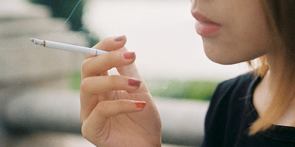 shallow focus photography of woman in black crew-neck top holding cigarette stick thumbnail