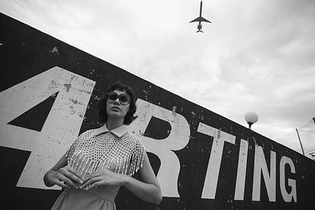 Grayscale Photo of Woman Standing Beside Wall thumbnail