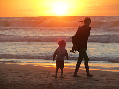 woman and boy on sand near body of water during golden hour thumbnail