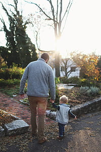 Man Holding Hands With Baby While Walking Through Pathway Facing Sunlight thumbnail