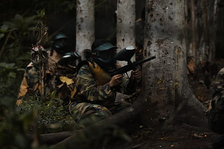 people with paintball guns hiding behind trees during day thumbnail