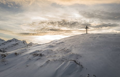 black cross on top of mountain covered snow at daytime thumbnail