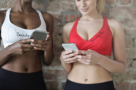 Two multi ethnic young women in sports bra looking at their mobile phones in a gym thumbnail