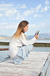 woman sitting on dock while holding smartphone thumbnail