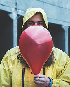 person in yellow hooded jacket holding red inflated balloon thumbnail