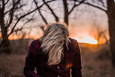 person wearing black and red plaid shirt with head down standing near trees during golden hour thumbnail