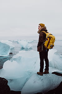 man standing on iceberg in in front of body of water thumbnail