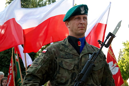 man holding rifle near red and white flag at daytime thumbnail