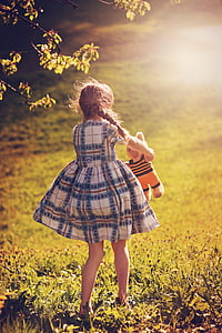 girl holding brown bear plush toy standing on grass fields thumbnail