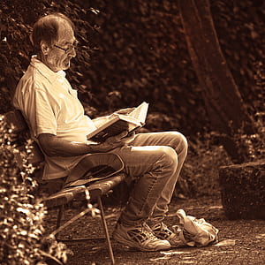 man sitting on bench while reading book thumbnail
