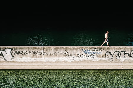 man walking on concrete fence near body of water thumbnail
