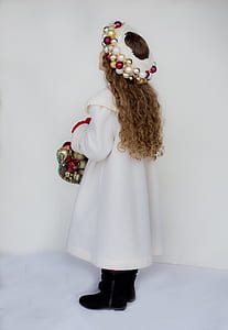 girl with brown curly hair wearing white gown carrying basket full of bauble thumbnail