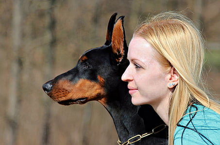 tilt shift photography of woman beside adult Doberman pinscher on outdoors thumbnail