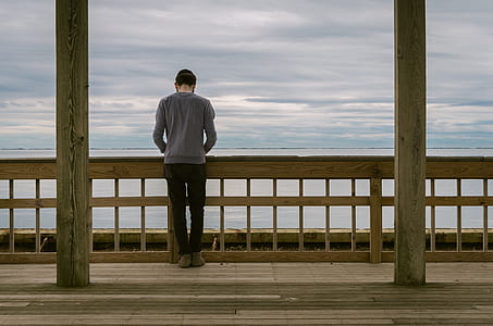 man leaning on wooden fence fronting ocean thumbnail