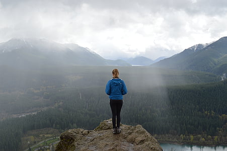 woman in blue hoodie and black bottoms standing on the edge of cliff thumbnail