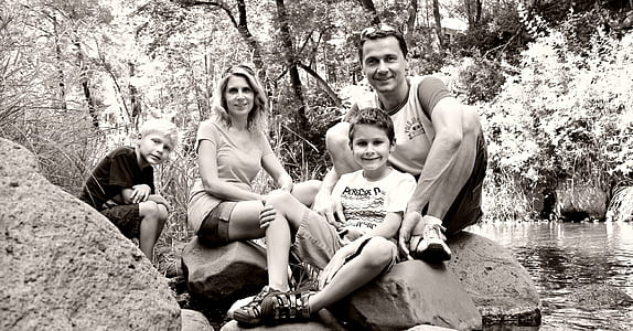 grayscale photo of woman, man, and two boys by water stream thumbnail