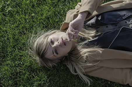 women's wearing brown coat lying on green grass field thumbnail
