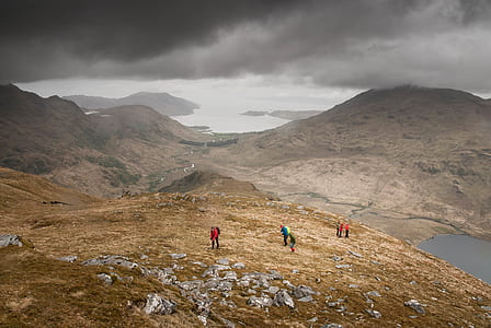 people standing on mountain overlooking body of water under cloudy skies thumbnail