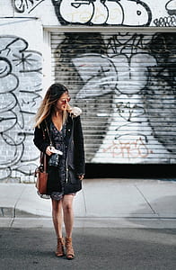 woman walking near white and black graffiti wall and shutter door thumbnail
