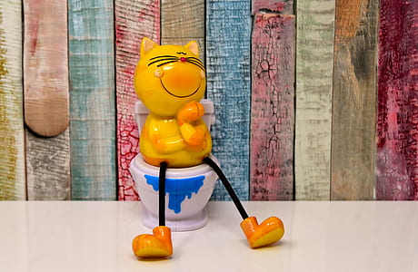 ceramic yellow cat sitting on toilet bowl figurine close-up photo thumbnail