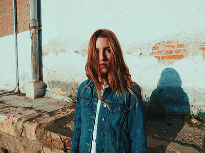 woman wearing blue denim jacket standing near green painted wall during daytime thumbnail