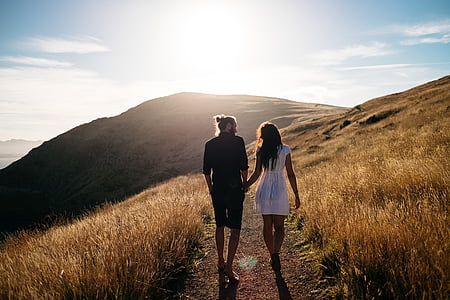 couples holding hands while walking on brown mountain at golden hour thumbnail