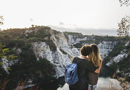 two person on hill top facing mountain with green leafed trees during daytime thumbnail