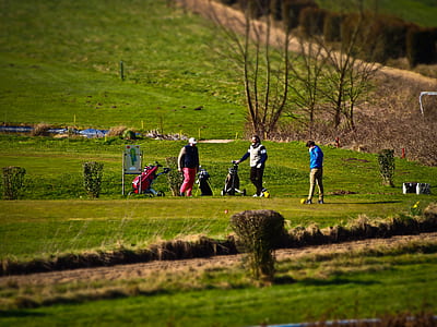 three men playing golf on field across hill during daytime thumbnail