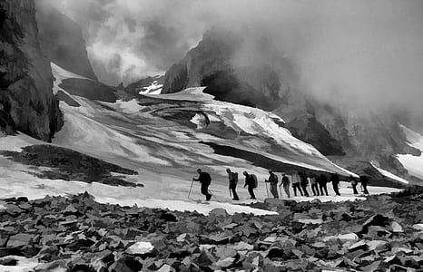 grayscale photography of group of men hiking up snowy mountain thumbnail