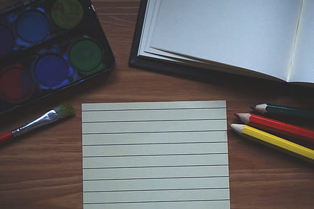 white paper between water color palette and color pencils on brown wooden surface thumbnail