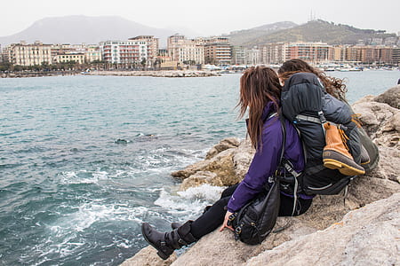 two women sitting on rock in front of body of water thumbnail