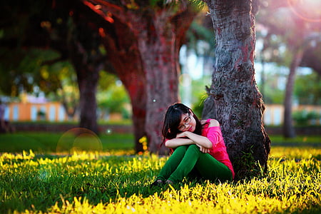 woman in pink cold-shoulder and green pants sitting on grass under brown tree during daytime thumbnail