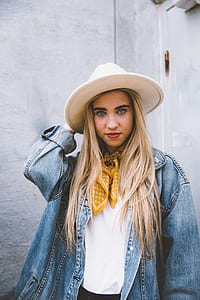 woman wearing blue denim jacket and white hat standing near white concrete wall thumbnail