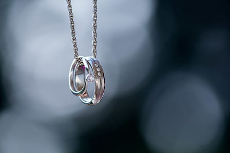 shallow focus photography of silver-colored necklace with two rings thumbnail