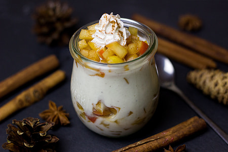 glass with cream and fruit cubes surrounded with cinnamon sticks on the table thumbnail