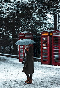 person holding umbrella while standing front of telephone booth thumbnail