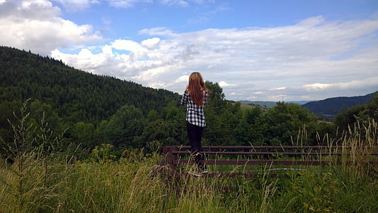 woman standing on fence while facing forest thumbnail