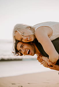 man carrying woman while smiling beside seashore thumbnail