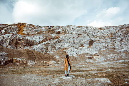 woman standing near brown cliff under cloudy sky thumbnail