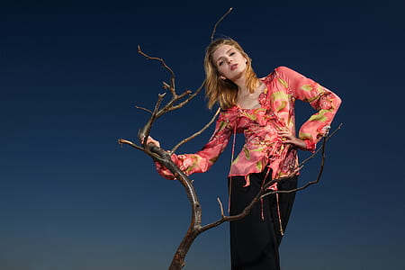 woman in pink and brown long-sleeved blouse standing beside brown tree branch thumbnail