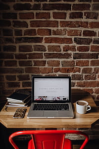 Creatives desk with laptop, camera, journals and books in front of brick wall thumbnail