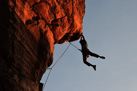 silhouette of man hanging on cliff under grey sky during daytime thumbnail
