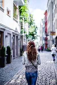 woman walking between concrete building during daytime thumbnail